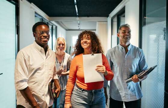 Diverse Group of Professionals Walking and Smiling in Office Corridor. They have just left a meeting and are all walking away happily with notebooks in their hands