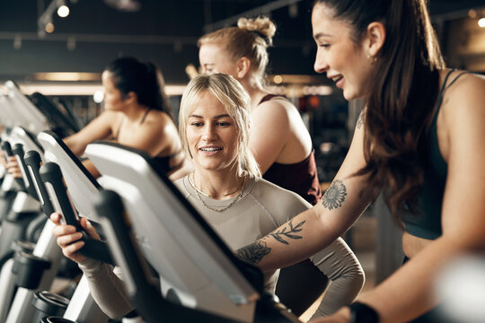 Smiling female instructor offering encouragement to a fit young woman riding a stationary bike during a cardio workout class in a gym