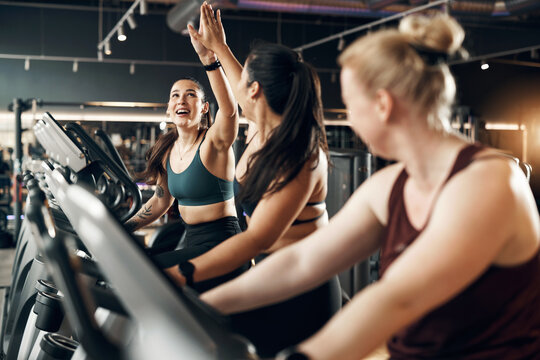 Ecstatic group of fit young women in sportswear laughing and high-fiving each other after a cardio exercise class on stationary bikes at the gym