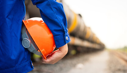 A worker is holding orange safety helmet with railway logistic trainsportation as backround.,...