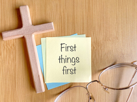 Praying Concept - First things first note written on paper with wooden cross background. Stock photo.