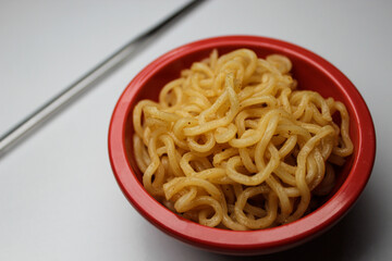 close-up of cooked wheat noodles in a small bowl with chopsticks isolated on a white backdrop