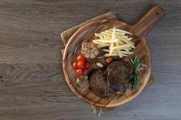 Thick, juicy grilled sirloin steak served with tomatoes and French fries on a wooden plate.