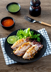 Fried squid with garlic and pepper in black plate on wooden table in seafood style.