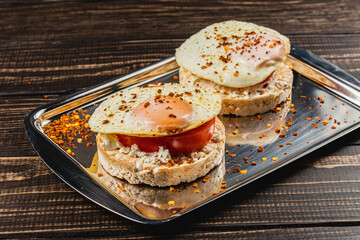 Freshly fried egg on rice bread with tomato and feta cheese on a metal tray
