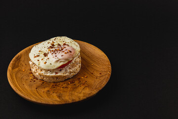 Egg on rice bread with tomato and cheese on a wooden plate on a black background