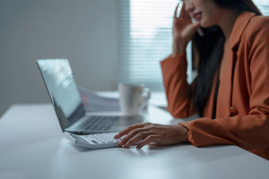 Businesswoman calculating financial data, analyzing statistics, and managing household expenses while using a calculator and laptop in a corporate office