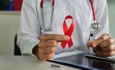 Health professional holding a red ribbon and a syringe to raise awareness for HIV/AIDS prevention...
