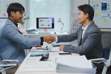 Two businessmen are shaking hands after reaching a successful business agreement in a bright and modern office, celebrating their collaboration and partnership