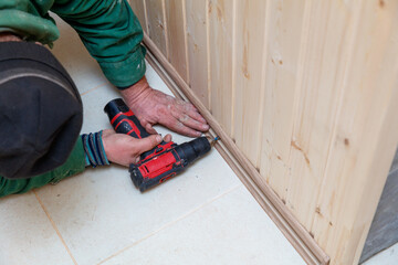 A man is using a power drill to make a hole in a wooden board
