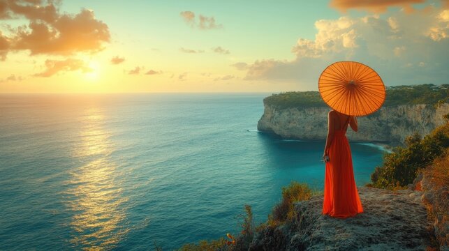 Stunning sunset panorama over a dramatic coastal cliff with a vibrant red umbrella silhouetted against the orange sky and serene ocean waters
