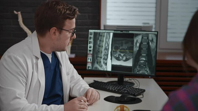 An experienced doctor, osteopath, conducts consultations in a modern clinic. A man consults a patient. The MRI image is open on the computer screen.