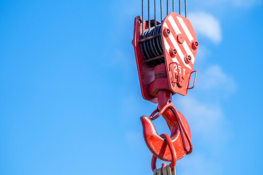 Red industrial crane hook against clear blue sky.