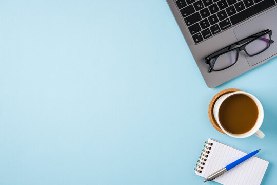 Coffee cup, laptop keyboard and various stationery items on blue office desk. Business office concept