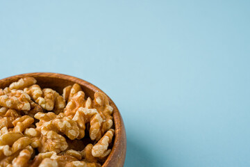 Top view of heap of walnut kernels in wooden bowl on blue background