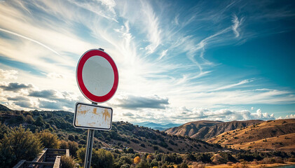 A red stop sign on a road with a blue sky and clouds in a desert mountain landscape