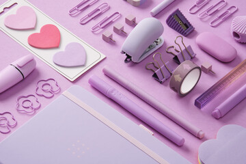 Stationery background with pastel purple supplies, notepad, paper clips, post-its, felt-tip pens, eraser, stapler, ruler, pins. Selective Focus.