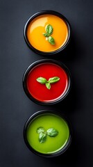 Three bowls of soup with different colors and a green leaf on top. The bowls are arranged in a row, with the green bowl in the middle and the red and yellow bowls on either side