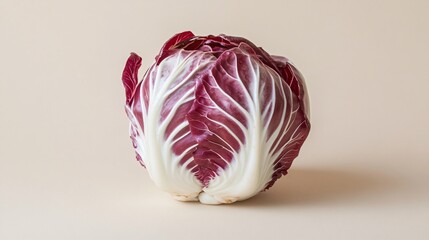 Fototapeta premium A fresh radicchio head, isolated on a neutral beige background, showcasing its vibrant color and crisp texture