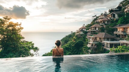 Infinity pool perched on a hillside with a young woman soaking in the ocean view