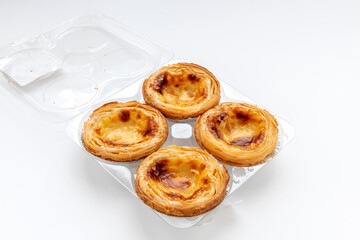 Four baked egg tarts in a plastic holder isolated on white.
