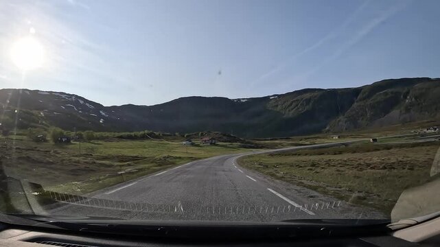 Driving along the E69 road in northern Norway's tundra. The barren landscape features moss, grass, and a few trees. The sea briefly appears on the right side, enhancing the remote beauty.