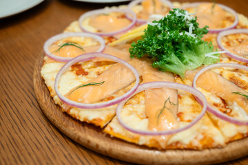 Fresh salmon pizza topped with shallot slices and lettuce, served in the restaurant