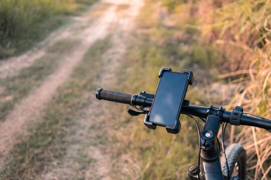 Smartphone and holder attached to the handlebar of a bicycle while riding on the rough dirt road in the field