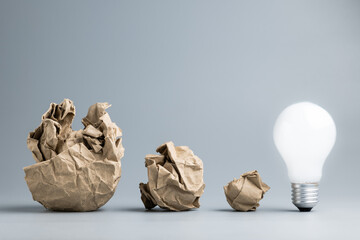 Different size of crumpled paper balls with a glowing light bulb at the end of the row, big...