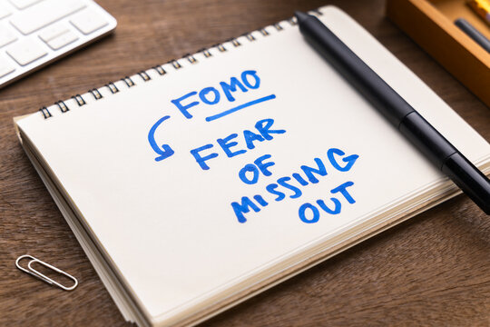 Closeup text Fear of Missing Out, or FOMO,  handwritten in the notepad on the desk