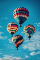 Obraz premium Four vibrant hot air balloons floating in a clear blue sky, showcasing bright patterns and colors.