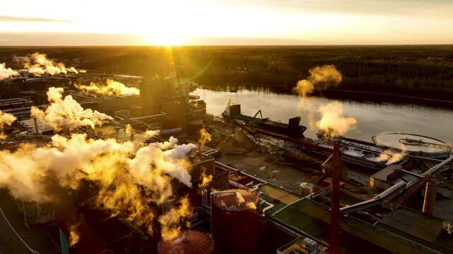 Pulp and paper mill emitting smoke at golden hour, aerial view