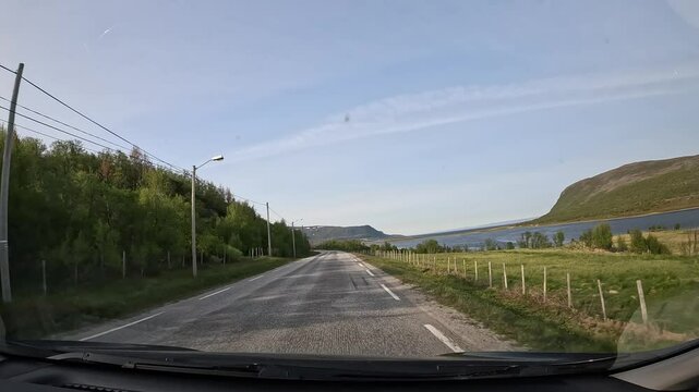 Driving through Norway's northern taiga on E69 highway. Low forest trees and a few houses line the road, with a view of the sea on the right. A peaceful, scenic journey through nature.