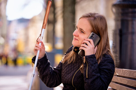 A visually impaired woman standing in city with a white cane and using her smartphone