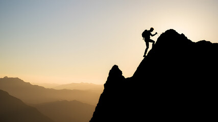 Silhouette of the climber who is climbing up the mountain against the ridge. Generative AI