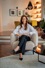 Fototapeta premium Brunette haired attractive woman sitting in an armchair in her modern home