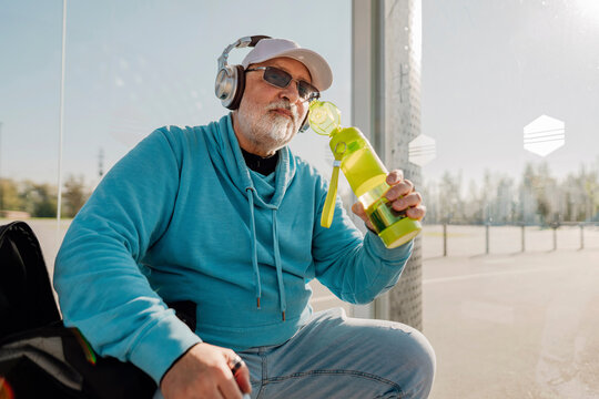 Smiling senior holding bottle and sitting at bus stop