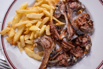 Plato y ración de chuletillas de lechazo, cordero joven, a la brasa con patatas fritas. Tradicional de Castilla y León, España