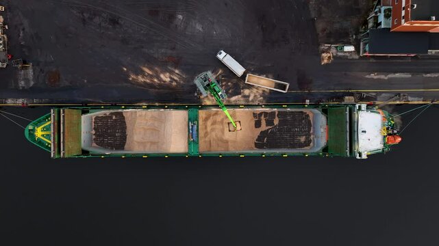 Crane loading wood chip on to cargo ship at industrial port paper mill