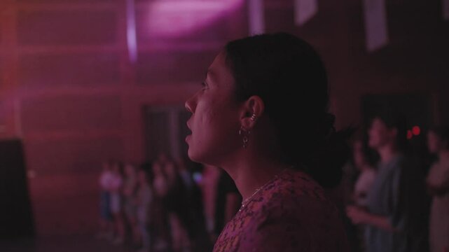Beautiful latin female singing at concert, staying with a crowd of people during musical festival, worship night at church, worshipping God Jesus, enjoying atmosphere with young people