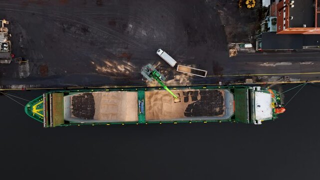 Crane loading wood chip onto barge at industrial port paer mill