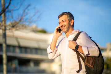 Smiling man talking on phone with backpack in urban setting