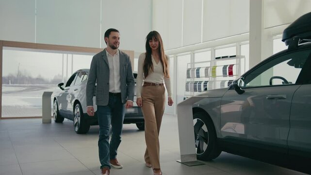 Camera view of Caucasian husband and wife walking inside of car dealership. Choosing vehicle. Communicating while looking around. Making difficult decision together. Comparing prices.