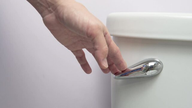 Female hand pressing the toilet handle in a bathroom