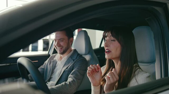 Funny female sitting in drivers seat. Exclaiming and laughing while trying out everything in new car. Manager sitting next to woman and smiling. Happy customer. Girl talking and asking questions.