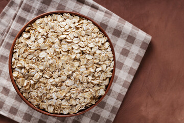 Raw Rolled Oats in Clay Bowl on Checkered Linen Napkin, Top View, Copy Space