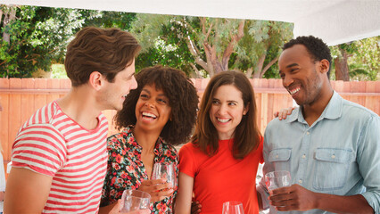 Group Of Smiling Young Friends Enjoying Summer Drinks Outdoors In Garden At Home