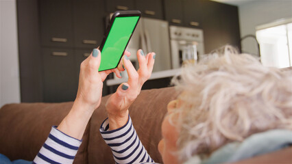 Senior Woman On Sofa At Home Using Green Screen Mobile Phone Browsing Online Or Checking Messages