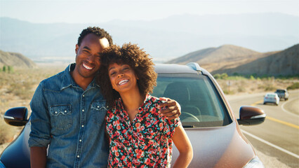 Portrait Of Smiling Young Couple On Road Trip Standing By Rental Car On Country Road