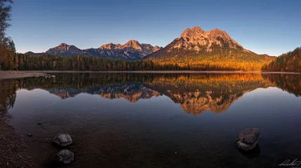 Calm lake reflecting autumnal mountains at sunrise.